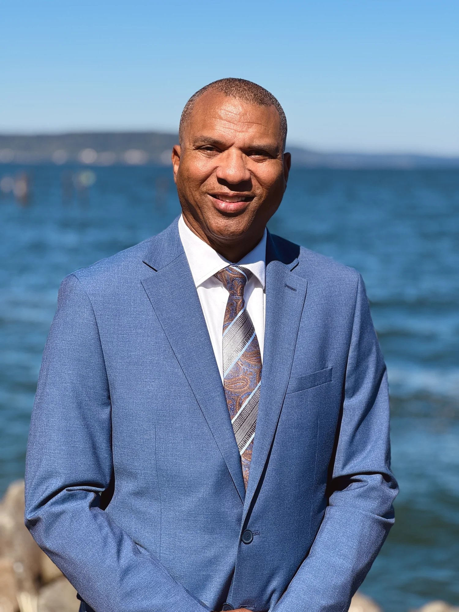 James Armstrong standing beside the waterfront in a blue suit